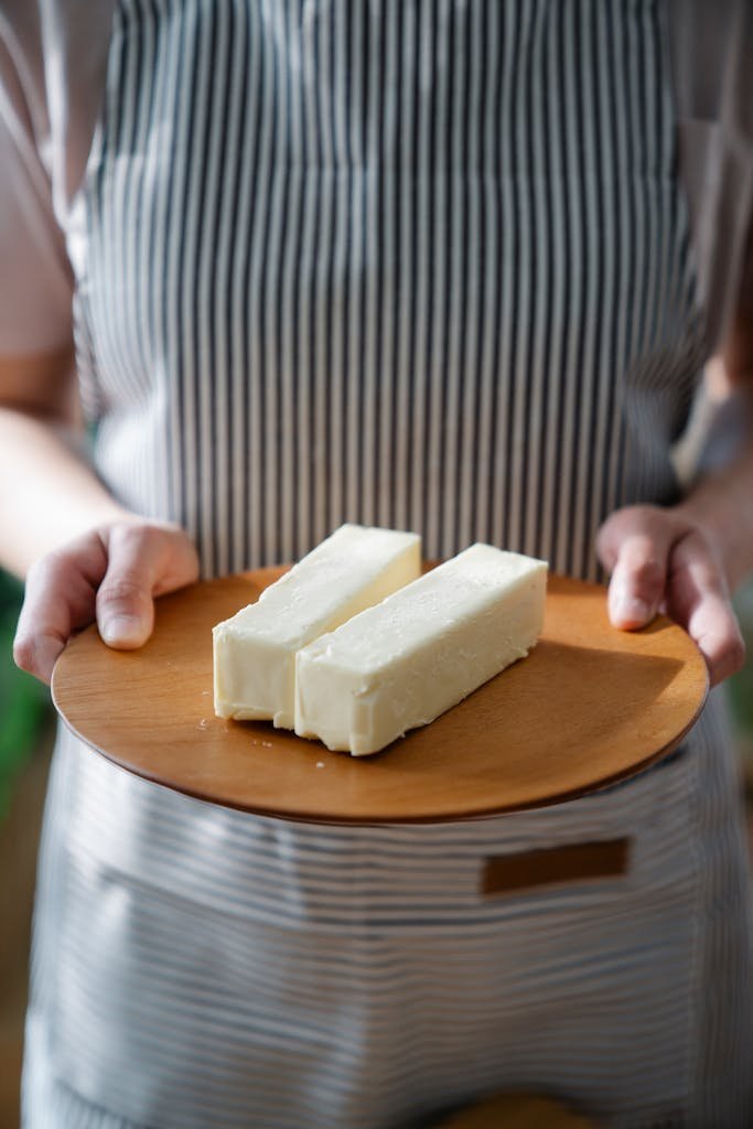 Close-up of a chef holding a wooden plate with two sticks of butter.